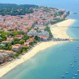 Vue aérienne d'une ville côtière avec une plage bondée et des bateaux dans l'eau.