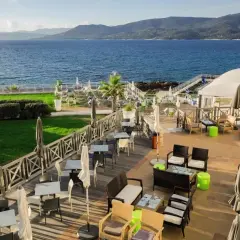 Terrasse d'un hôtel avec vue sur la mer, mobilier extérieur et verdure.
