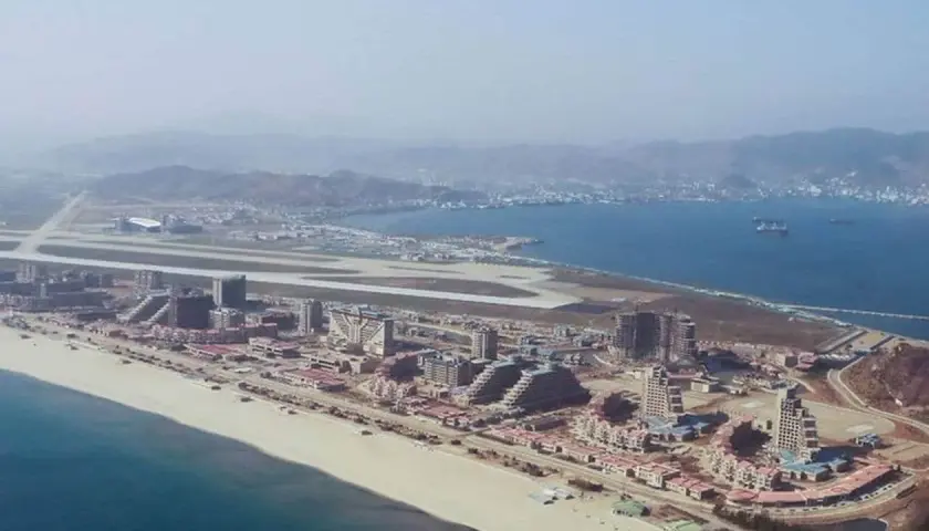 Vue aérienne d'une station balnéaire en construction en Corée du Nord, avec des bâtiments modernes, une plage et un aéroport.