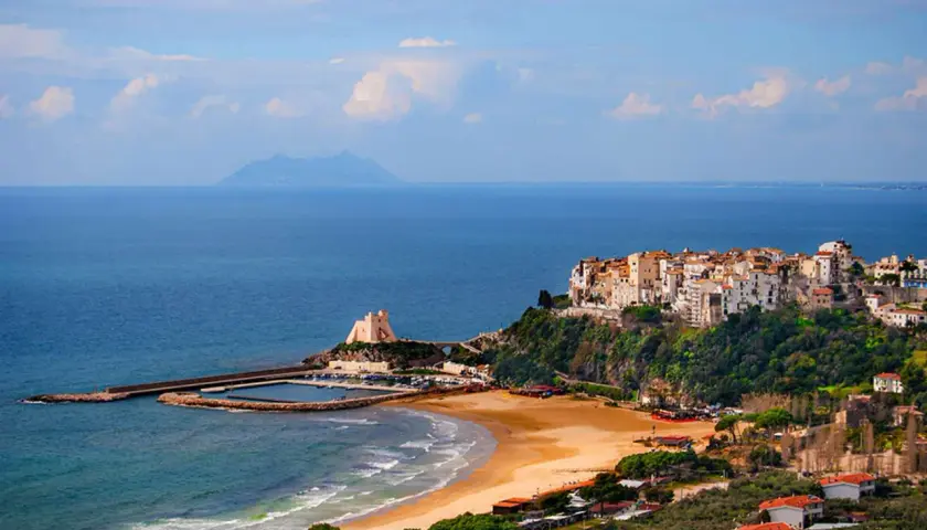 Vue d'une ville côtière italienne perchée sur une falaise, avec une plage et un port en contrebas.