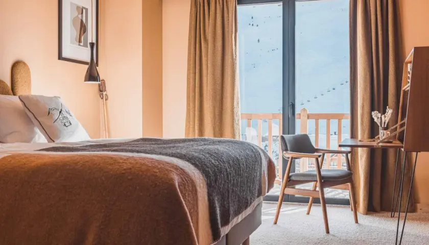 Chambre d'hôtel avec lit douillet, vue sur les montagnes enneigées et télécabines.