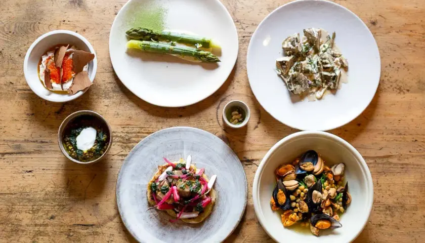 Assortiment de plats gastronomiques : asperges, moules, tartare, et autres mets fins sur table en bois.