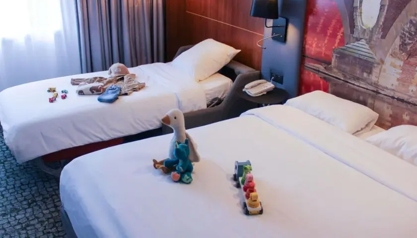 Chambre d'hôtel avec deux lits, jouets et vêtements pour enfants.