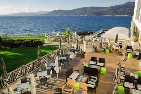 Terrasse d'un hôtel avec vue sur la mer, mobilier extérieur et verdure.